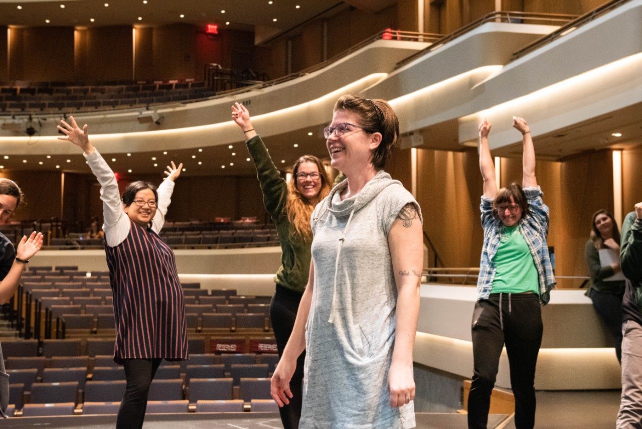 Allison standing in a circle of other people playing a theatre game