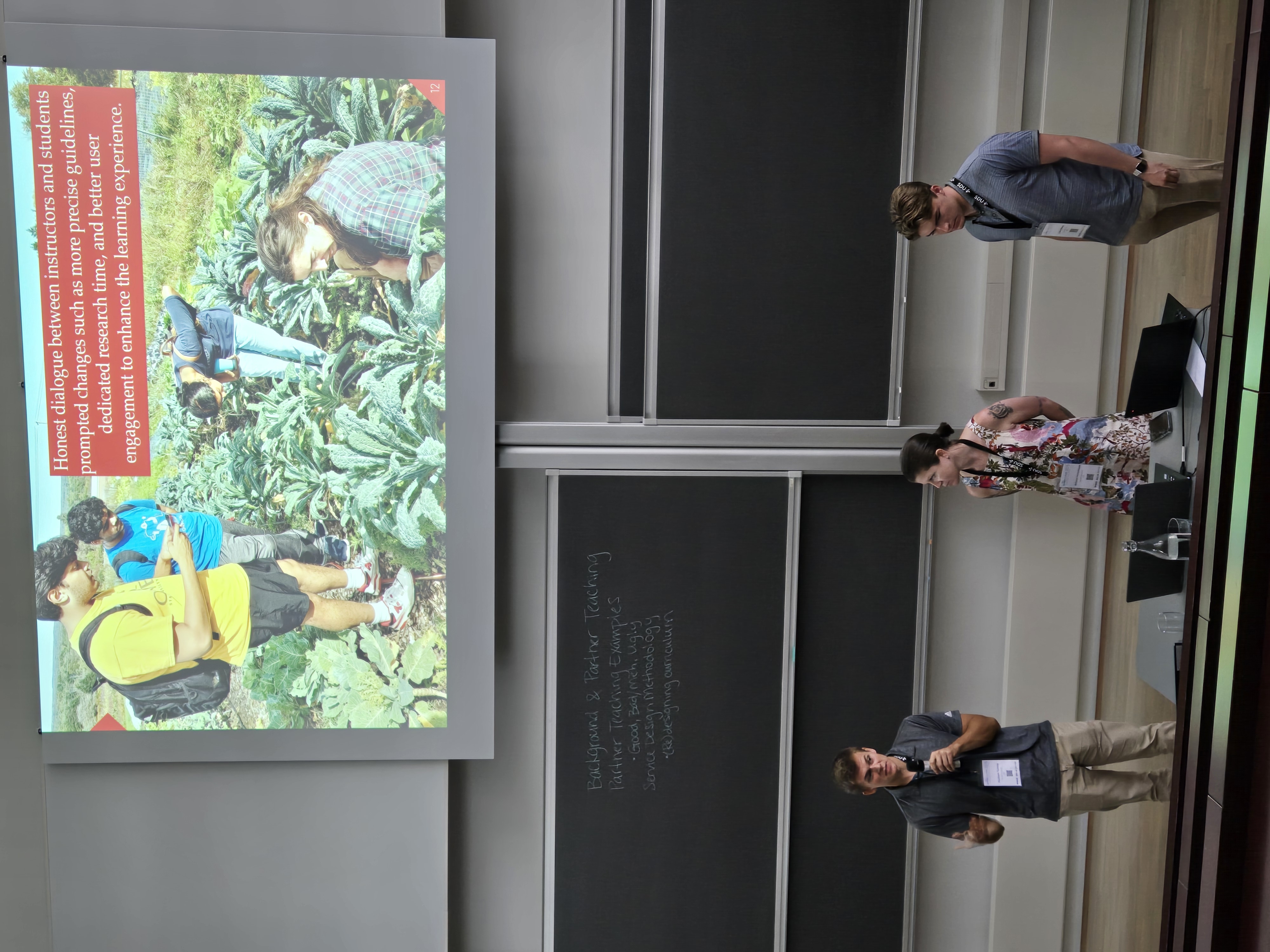 two white men stand on either side of a white woman, presenting under a large slide projection